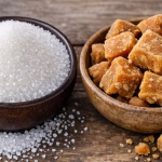 Close-up shot of refined sugar in one bowl and jaggery pieces in anothe